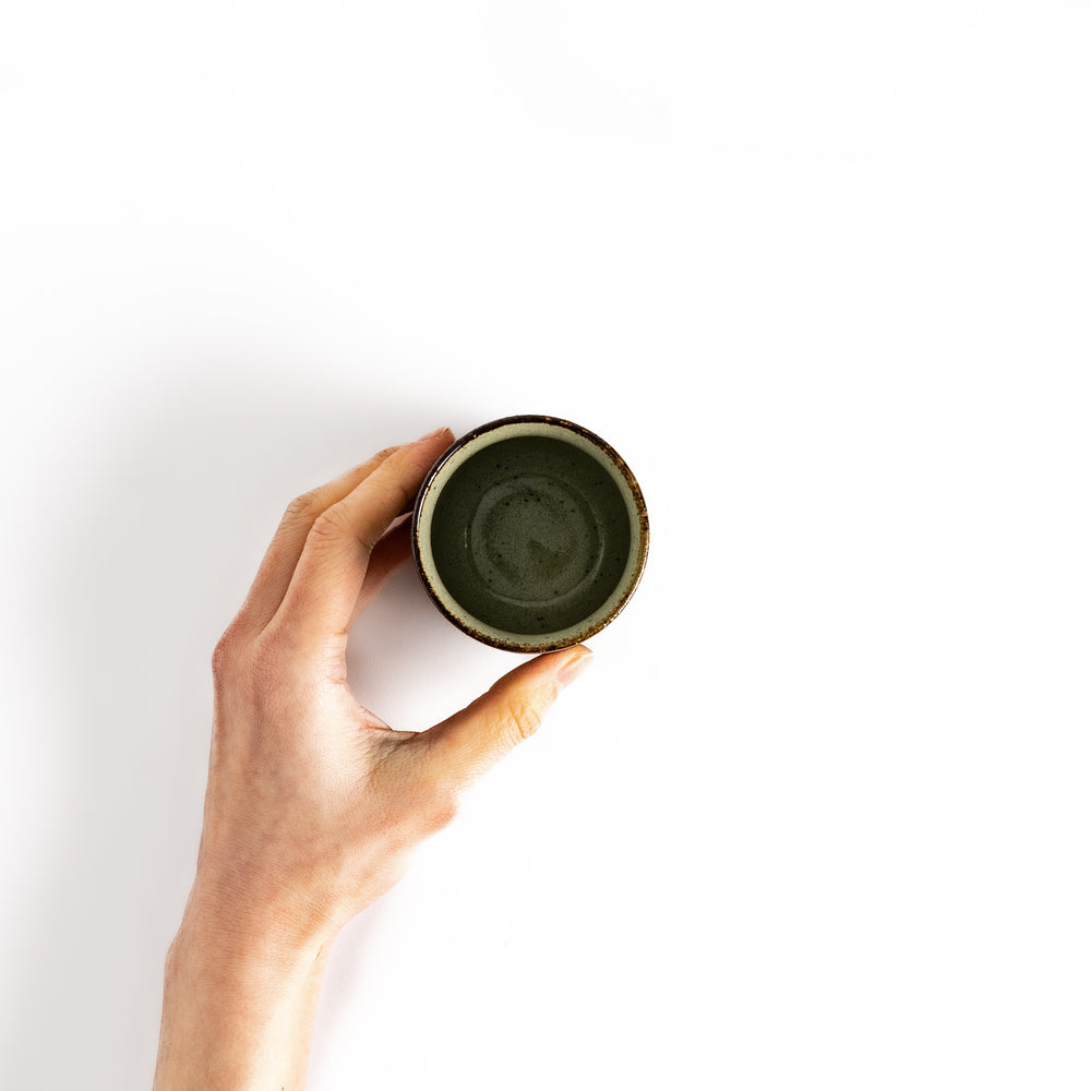 Hand holding a small, rustic teacup with a dark brown glaze, perfect for enjoying a traditional cup of tea.