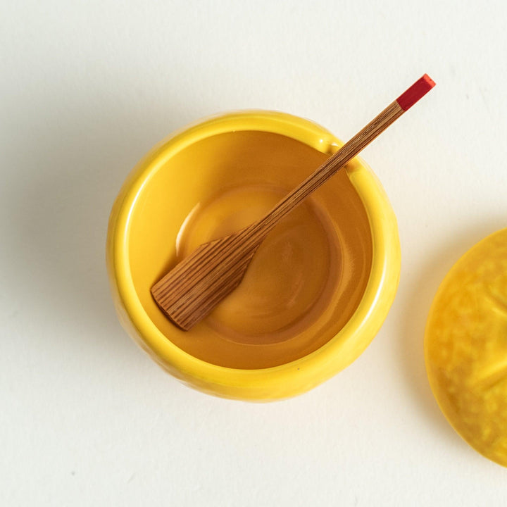 A small ceramic container shaped like a yuzu fruit with a lid and a spoon, bright yellow color.