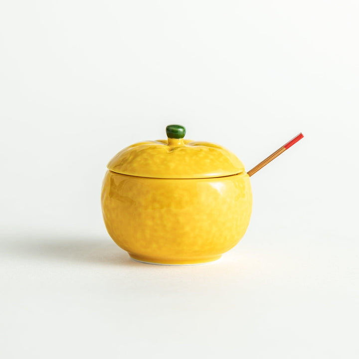 A small ceramic container shaped like a yuzu fruit with a lid and a spoon, bright yellow color.