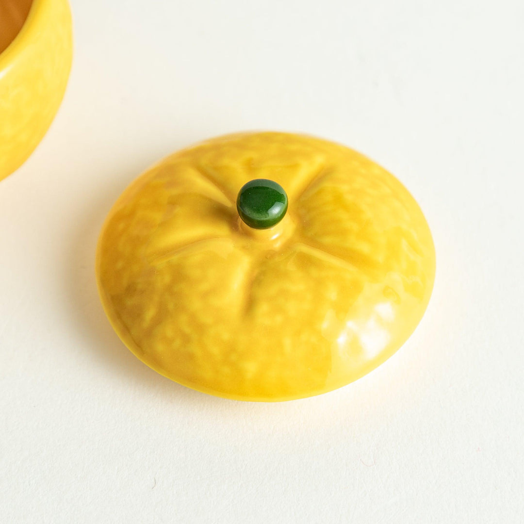 A small ceramic container shaped like a yuzu fruit with a lid and a spoon, bright yellow color.