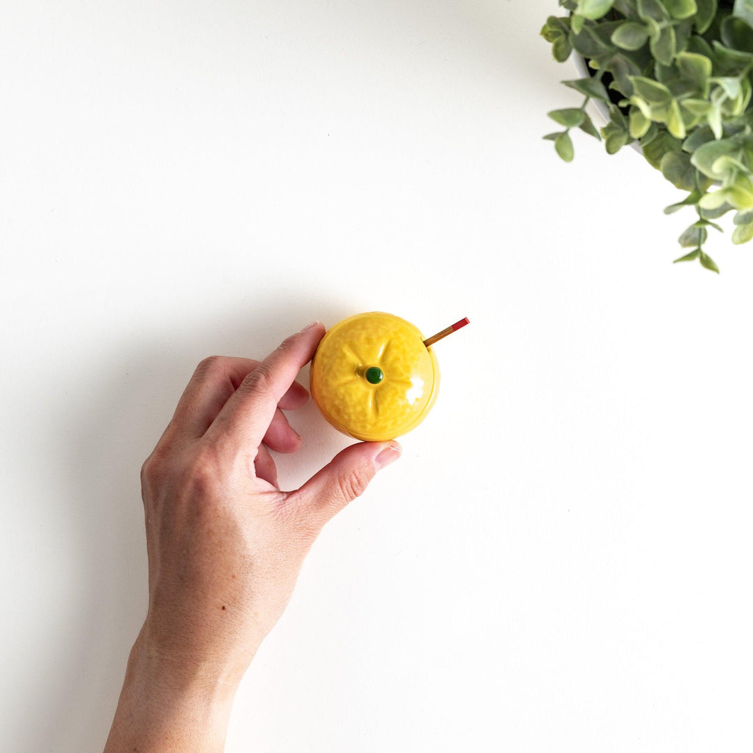 A small ceramic container shaped like a yuzu fruit with a lid and a spoon, bright yellow color.