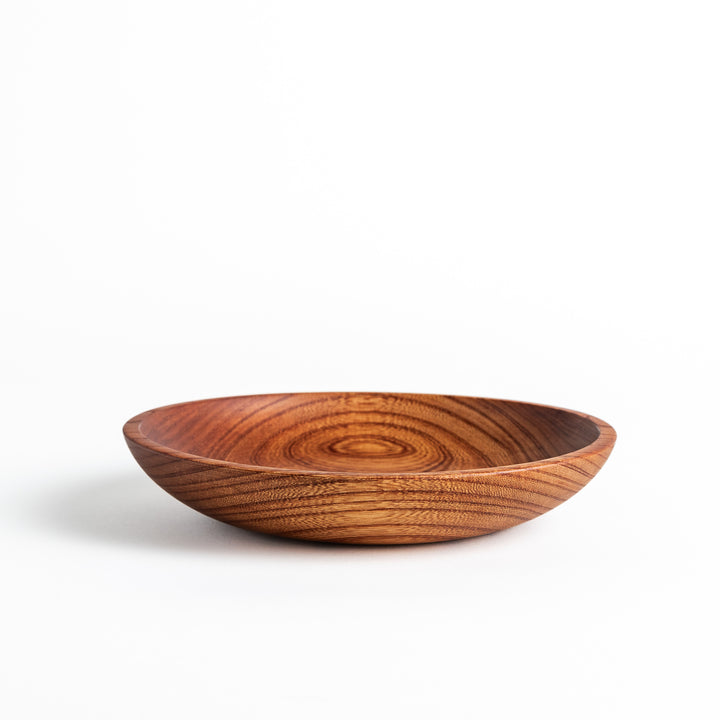 Close-up of a Zelkova wood salad plate with a smooth, polished finish and distinct wood grain pattern, captured from above.