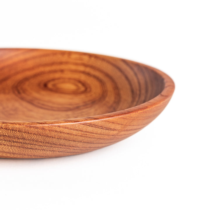 Close-up of the edge of a Zelkova wood salad plate, highlighting the smooth surface and unique swirling grain pattern.