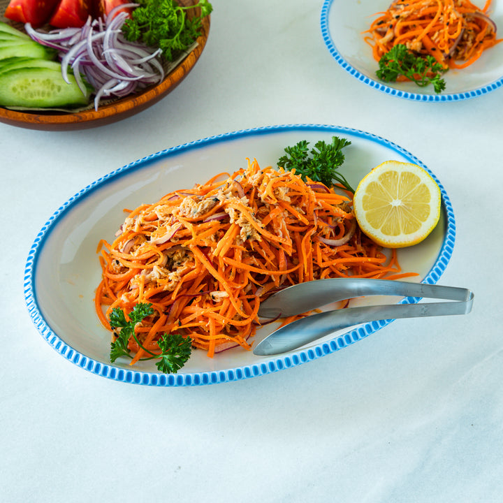 Carrot tuna salad served on a rustic scallop-edged white luncheon plate, garnished with parsley and lemon, showcasing the plate's blue beaded rim.