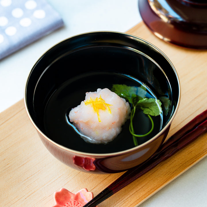 A bowl of Ebi Shinjo, a Japanese shrimp and vegetable dish, served in a black bowl with a touch of citrus zest and fresh herbs, perfect for a refined meal.