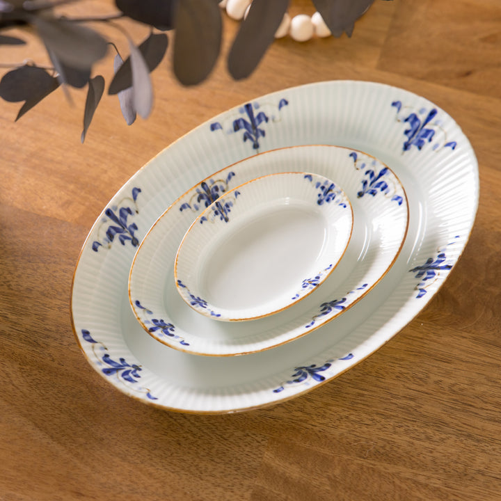 Three-piece oval plate set arranged on a wooden table, showcasing a ridged design and blue floral motifs on the plates, elegantly stacked.