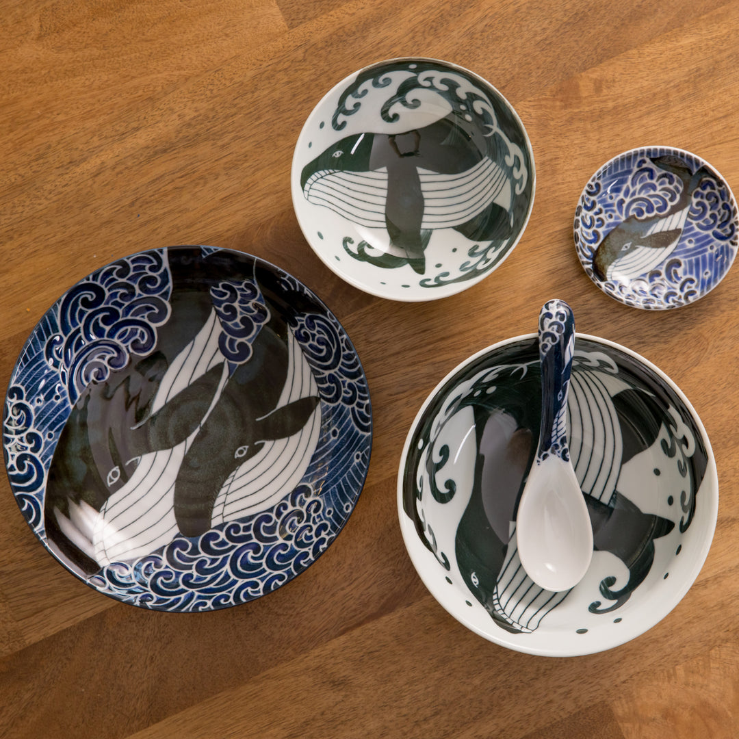 Whale-themed ceramic set featuring a large plate, two bowls, and a small dish, each with intricate whale and wave designs, on a wooden table.