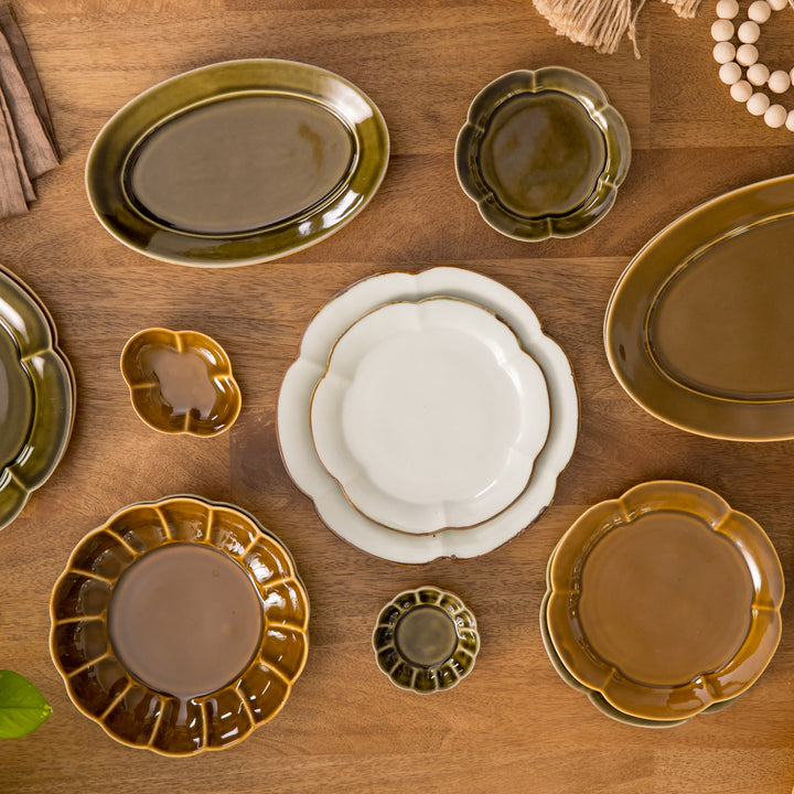 Assorted ceramic plates in varying floral shapes, featuring earthy brown and olive green tones, arranged on a wooden surface with decorative beads and leaves.