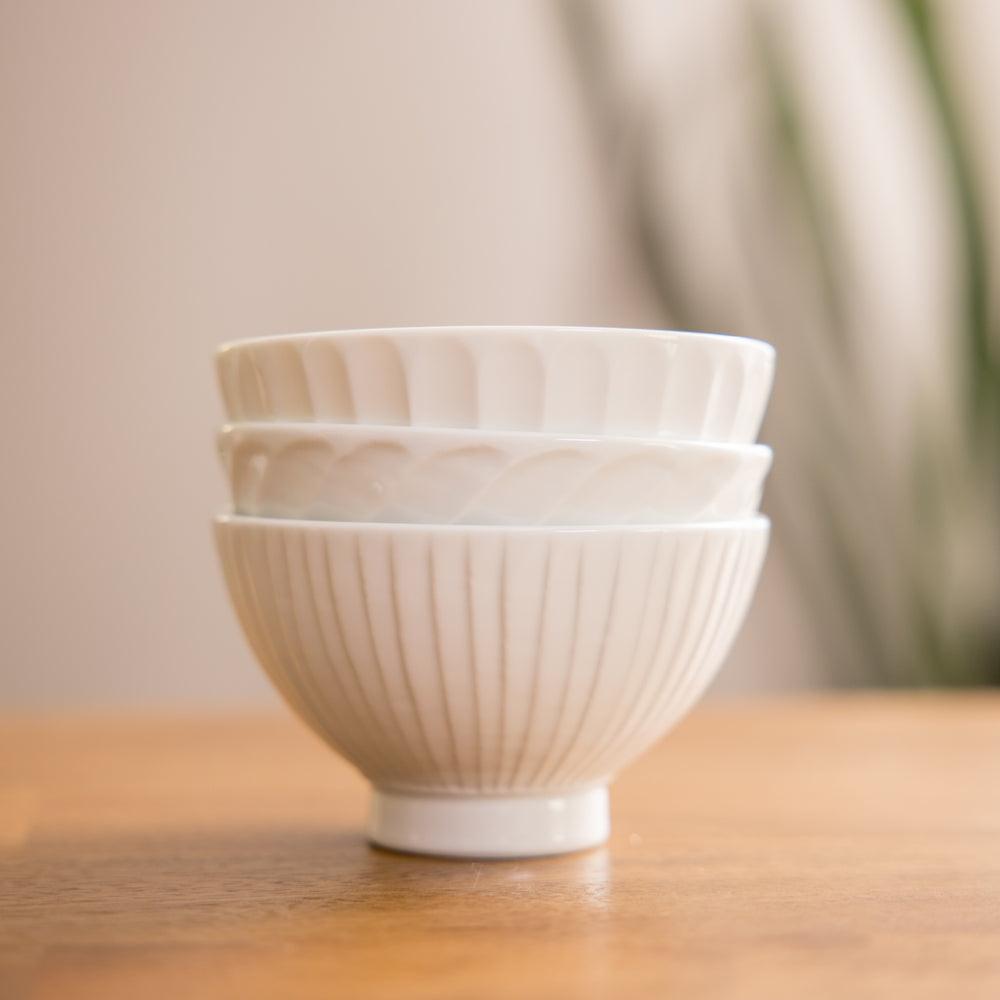 Three stacked white ceramic bowls with textured patterns, including ribbed and fluted designs, resting on a wooden surface.