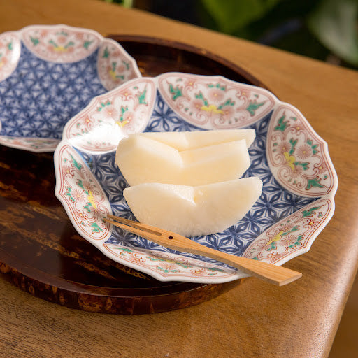 Two decorative dessert plates featuring intricate floral designs in blue and pink, with slices of pear placed on one plate.