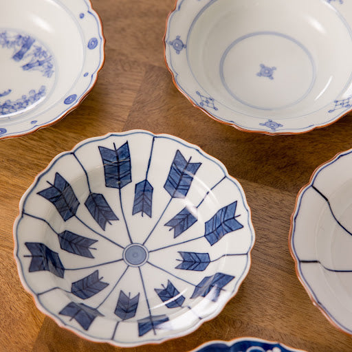 Arrow Feather Scalloped Rim Cereal Bowl featuring a central pattern of blue arrow motifs, surrounded by delicate blue scalloped rim details, set on a wooden surface.