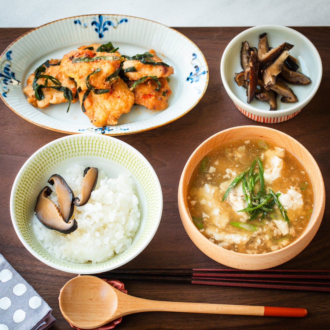 Japanese ceramic bowls and plates, featuring a floral-patterned plate for fried chicken, a green bowl for rice, and a wooden bowl for tofu soup.