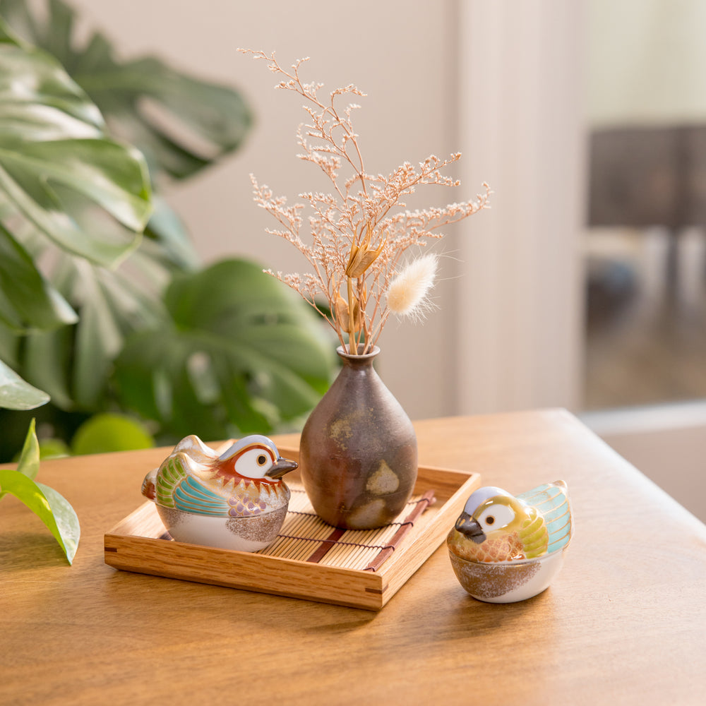 Two small bird-shaped bowls on a wooden tray, with a decorative vase holding dried flowers in the background. A charming addition to any table setting.