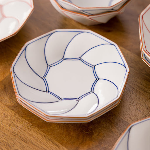 A close-up view of stacked octagonal dessert plates featuring a geometric blossom rim design in blue, highlighting their elegant shape and intricate detailing on a wooden table