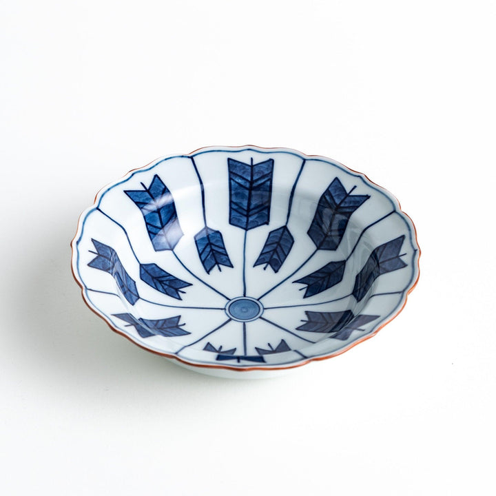 A ceramic bowl featuring a blue arrow feather pattern and scalloped edges.