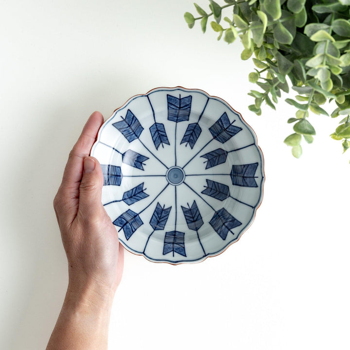 A ceramic bowl featuring a blue arrow feather pattern and scalloped edges.