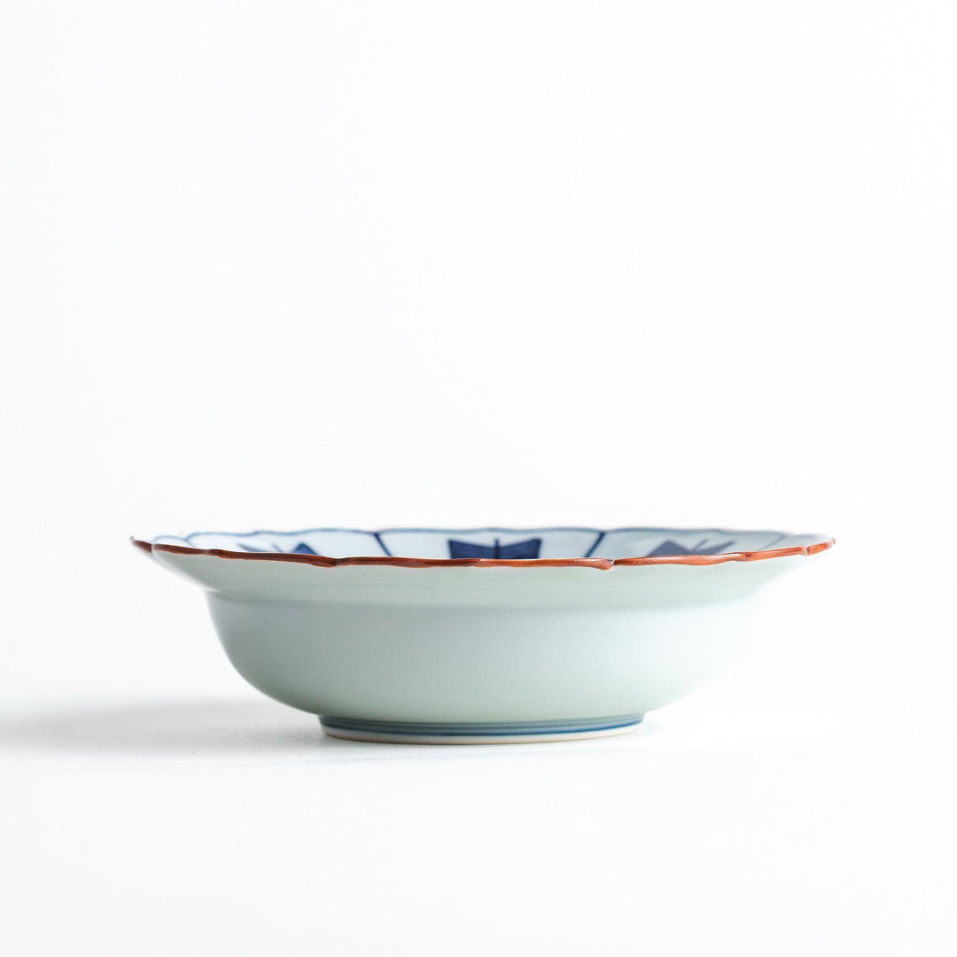 A ceramic bowl featuring a blue arrow feather pattern and scalloped edges.