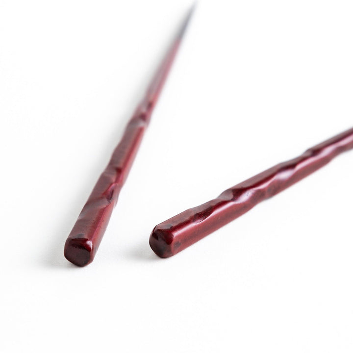 A pair of twisted wooden chopsticks in a dark red and black color gradient.