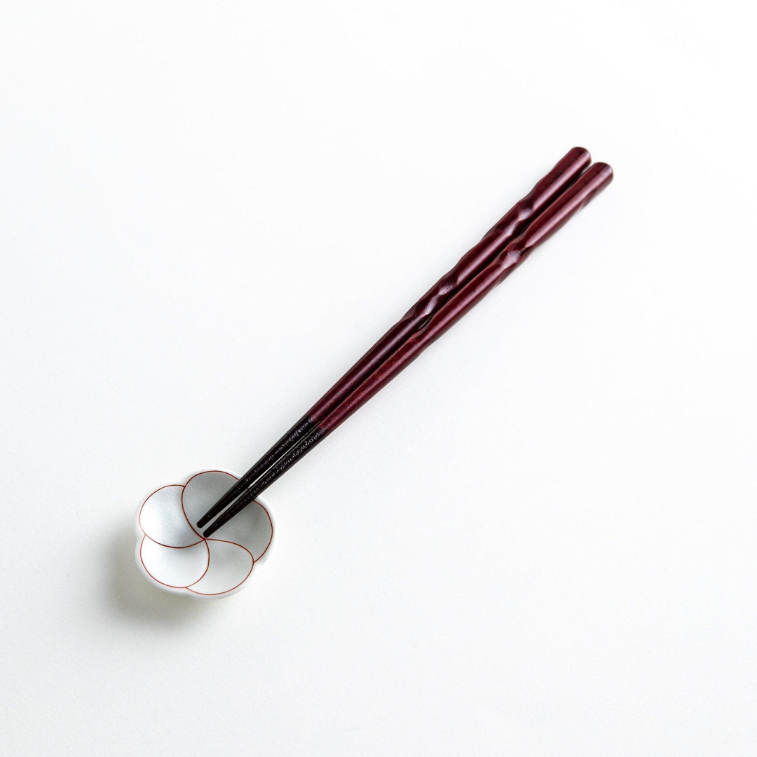 A pair of twisted wooden chopsticks in a dark red and black color gradient.