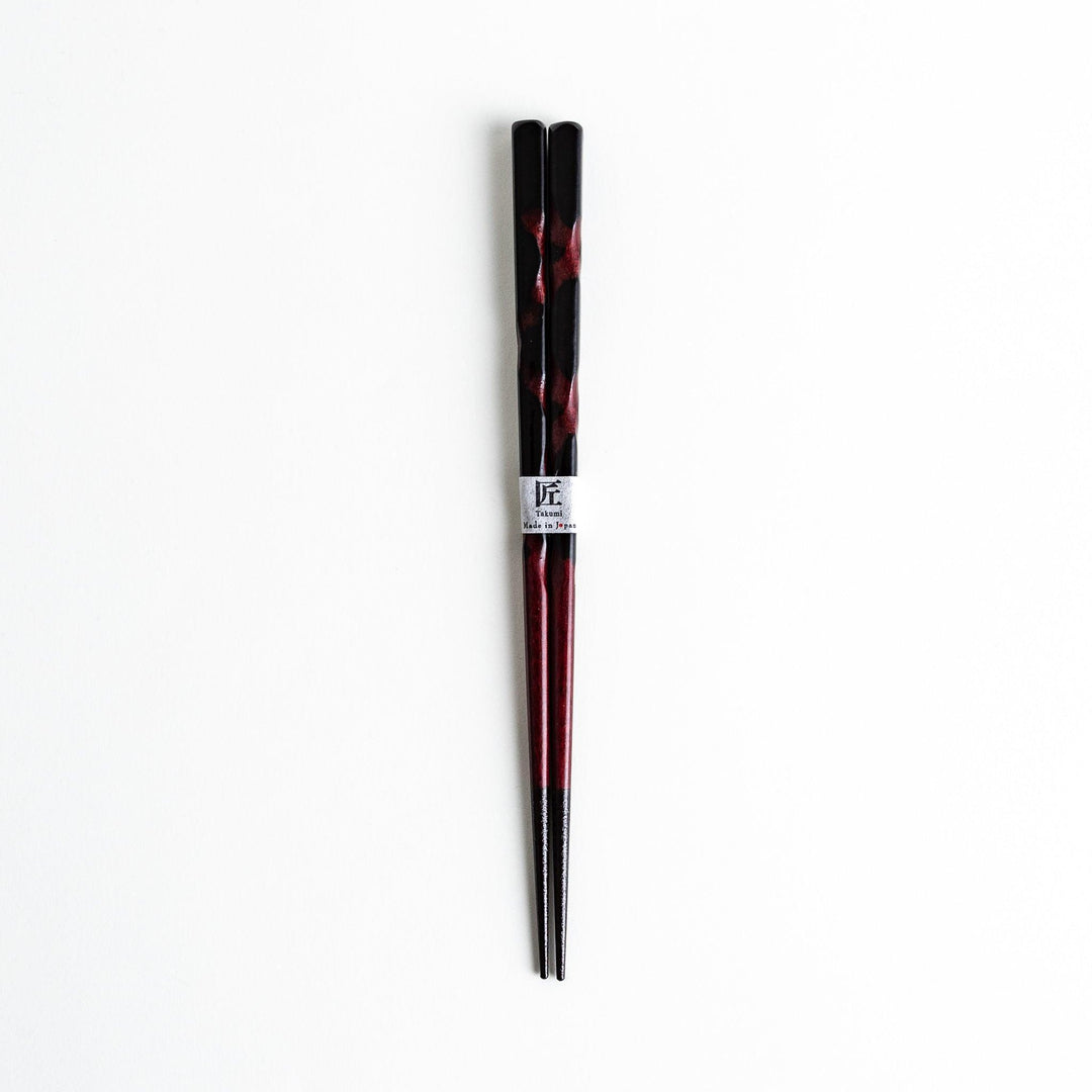 A pair of twisted wooden chopsticks in a dark red and black color gradient.