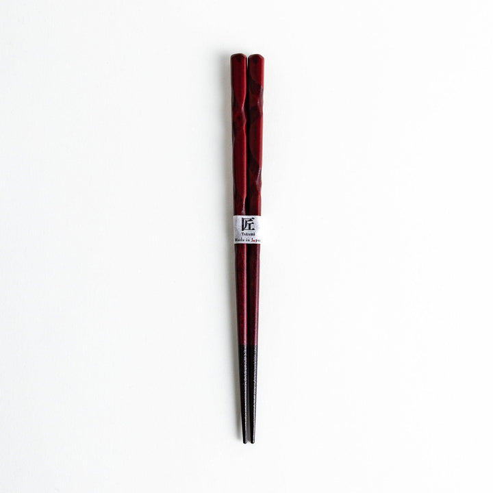 A pair of twisted wooden chopsticks in a dark red and black color gradient.