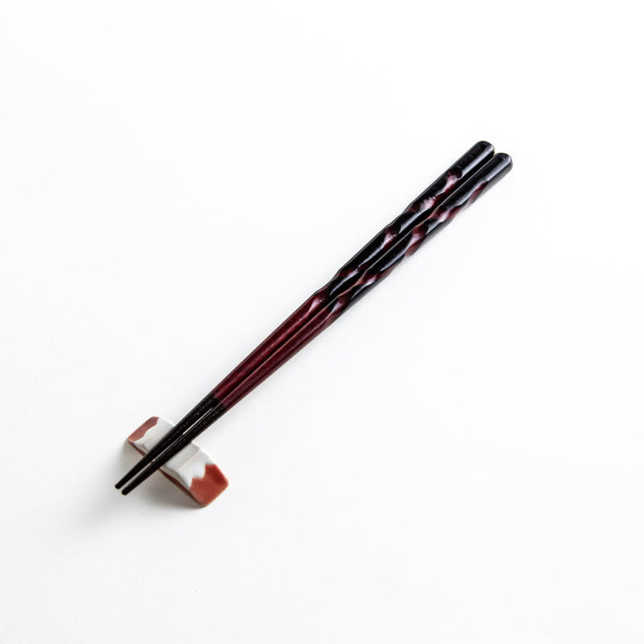 A pair of twisted wooden chopsticks in a dark red and black color gradient.