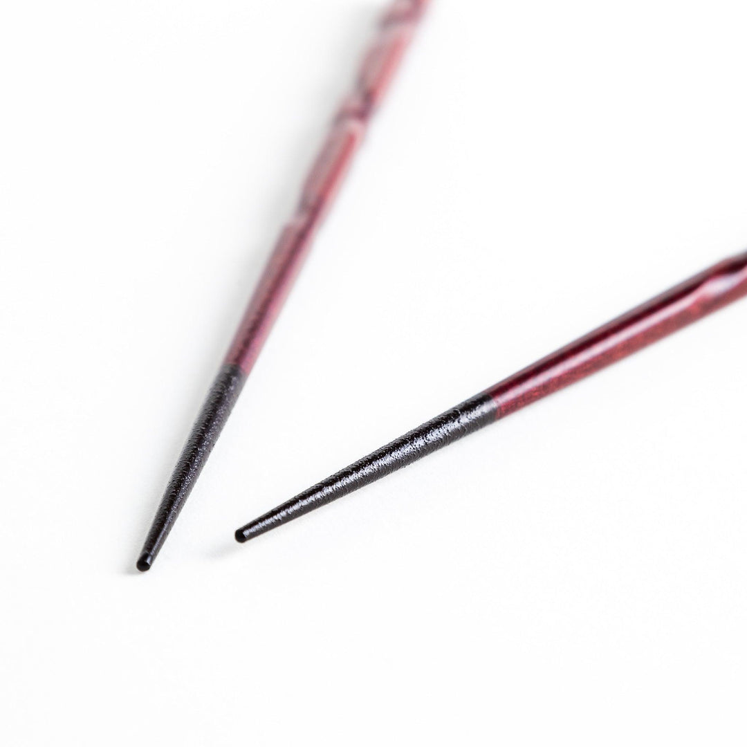 A pair of twisted wooden chopsticks in a dark red and black color gradient.