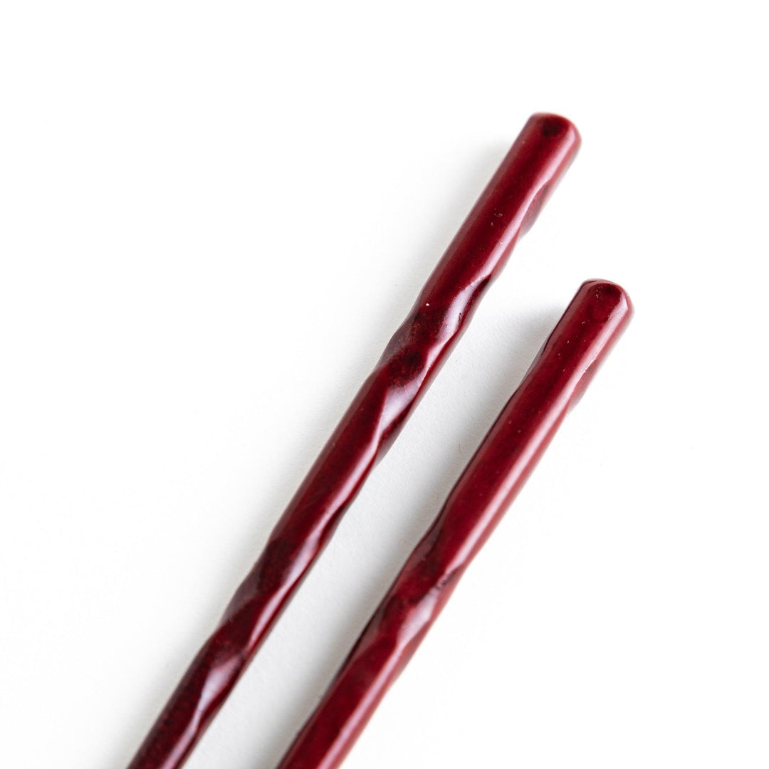 A pair of twisted wooden chopsticks in a dark red and black color gradient.