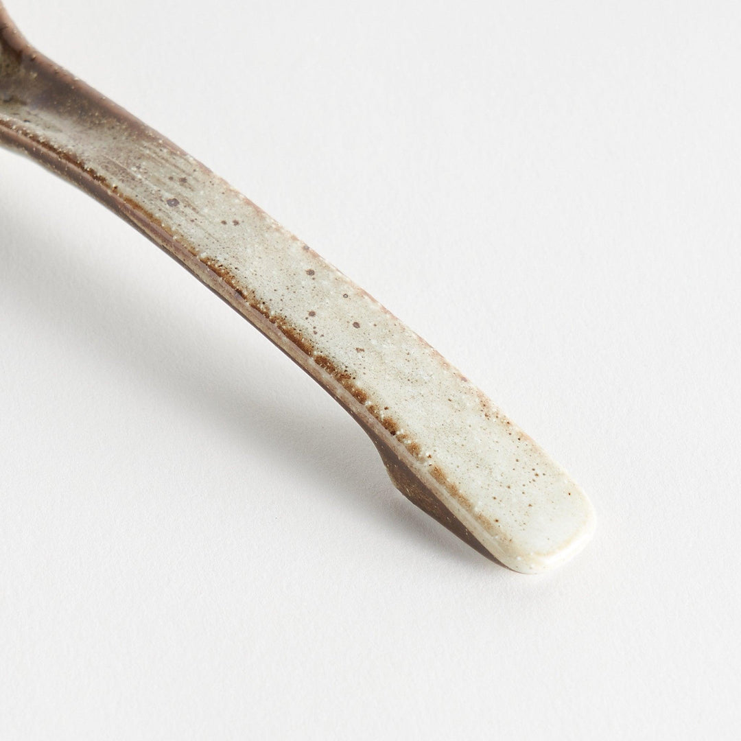 A matching light gray, textured and speckled ceramic spoon.