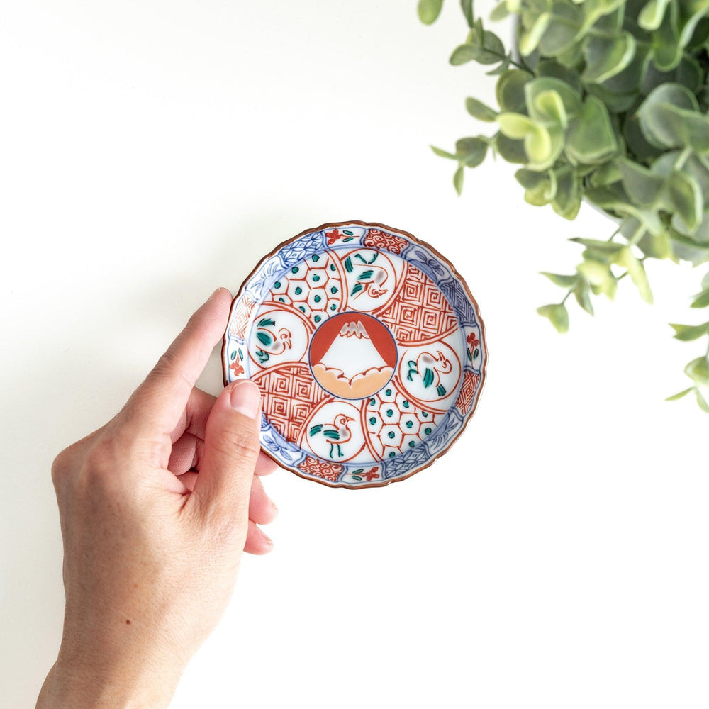 A vibrant ceramic dish with intricate patterns in blue, red, and green, centering around a depiction of Mount Fuji.