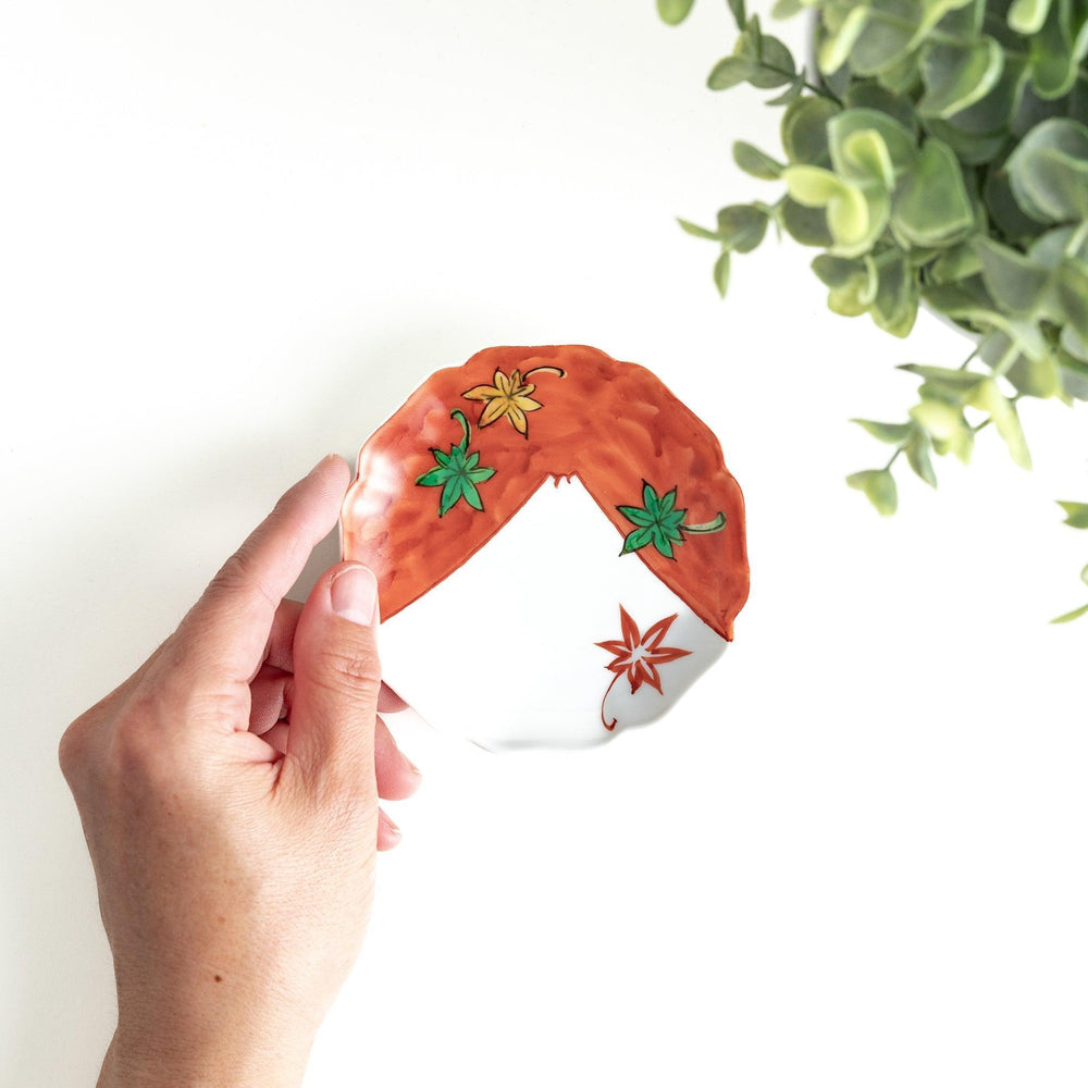 A white dish with a bright red border Mount Fuji, decorated with colorful maple leaves in red, yellow, and green.