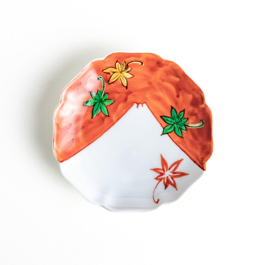 A white dish with a bright red border Mount Fuji, decorated with colorful maple leaves in red, yellow, and green.