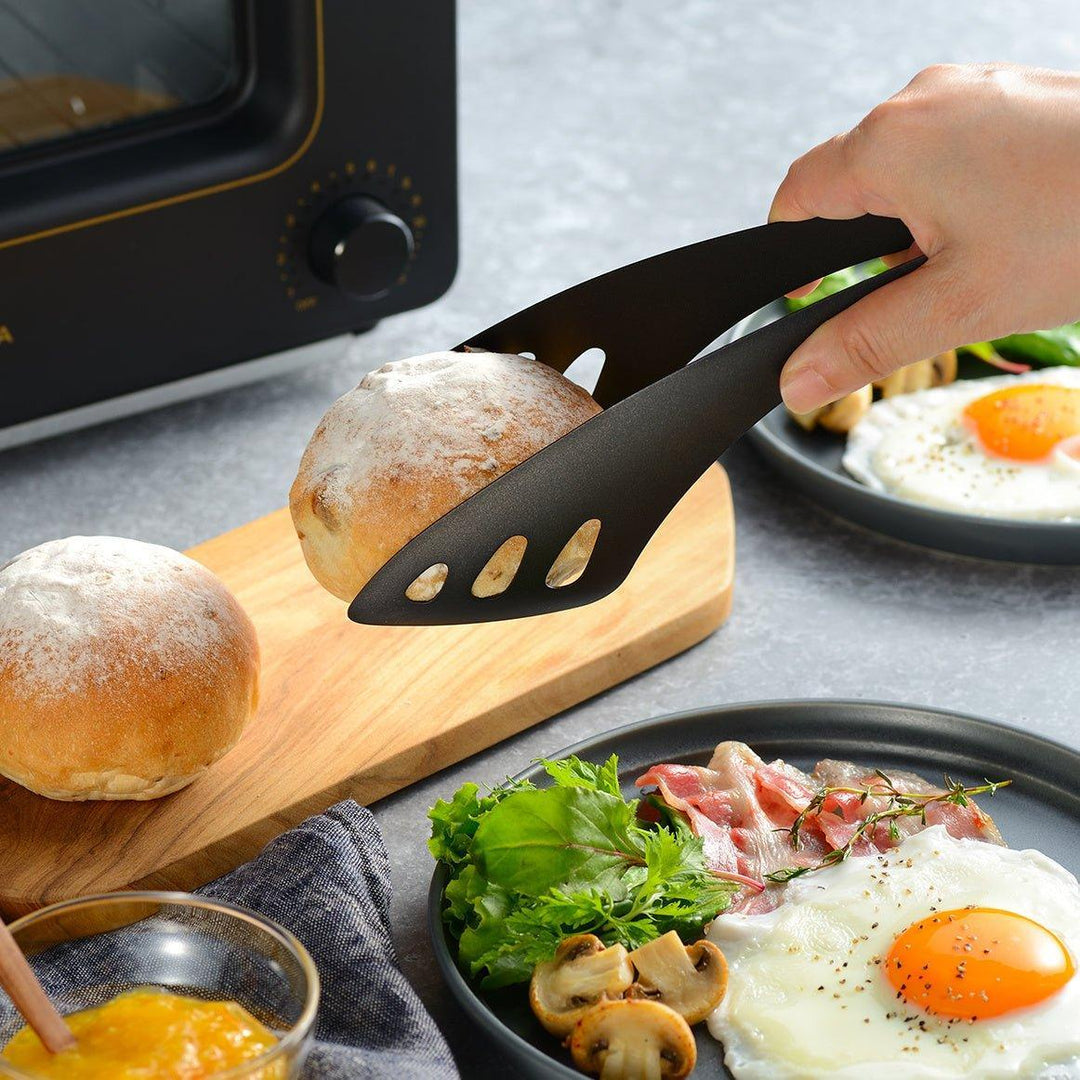 Matte black serving tongs with curved tips and a sturdy design, featuring small holes for draining or straining when serving.