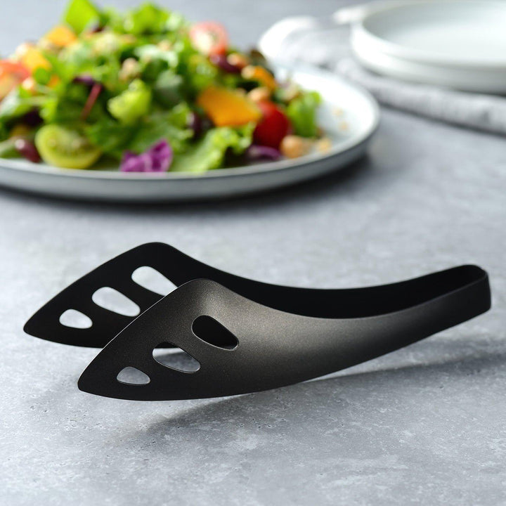 Matte black serving tongs with curved tips and a sturdy design, featuring small holes for draining or straining when serving.