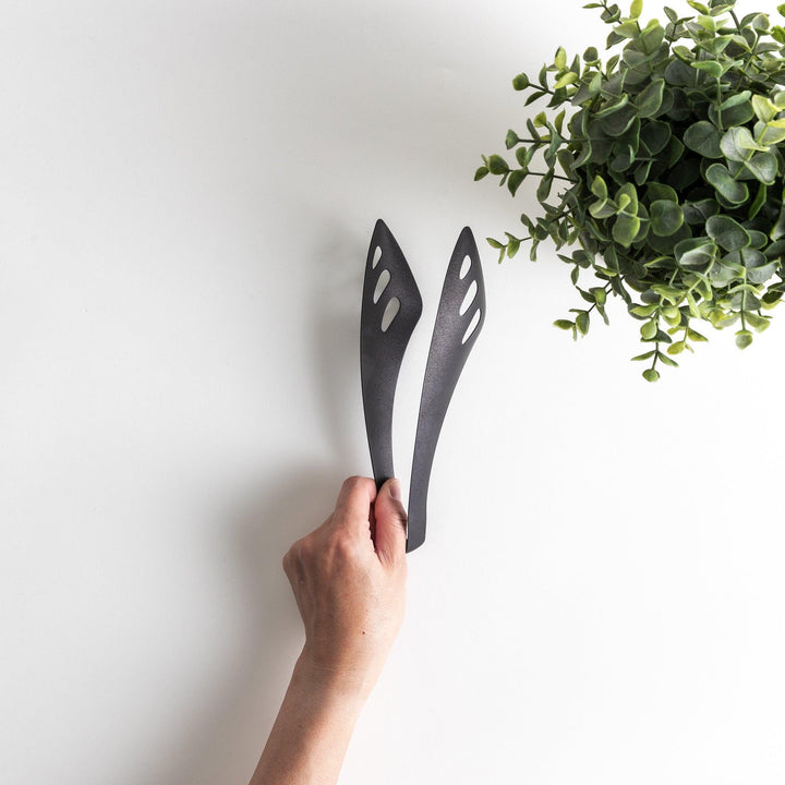 Matte black serving tongs with curved tips and a sturdy design, featuring small holes for draining or straining when serving.