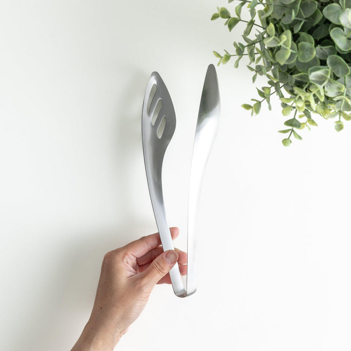 Sleek and modern stainless steel tongs with a slotted spoon end for draining and a solid spoon end for serving, perfect for handling salads, pasta, and other dishes with ease.