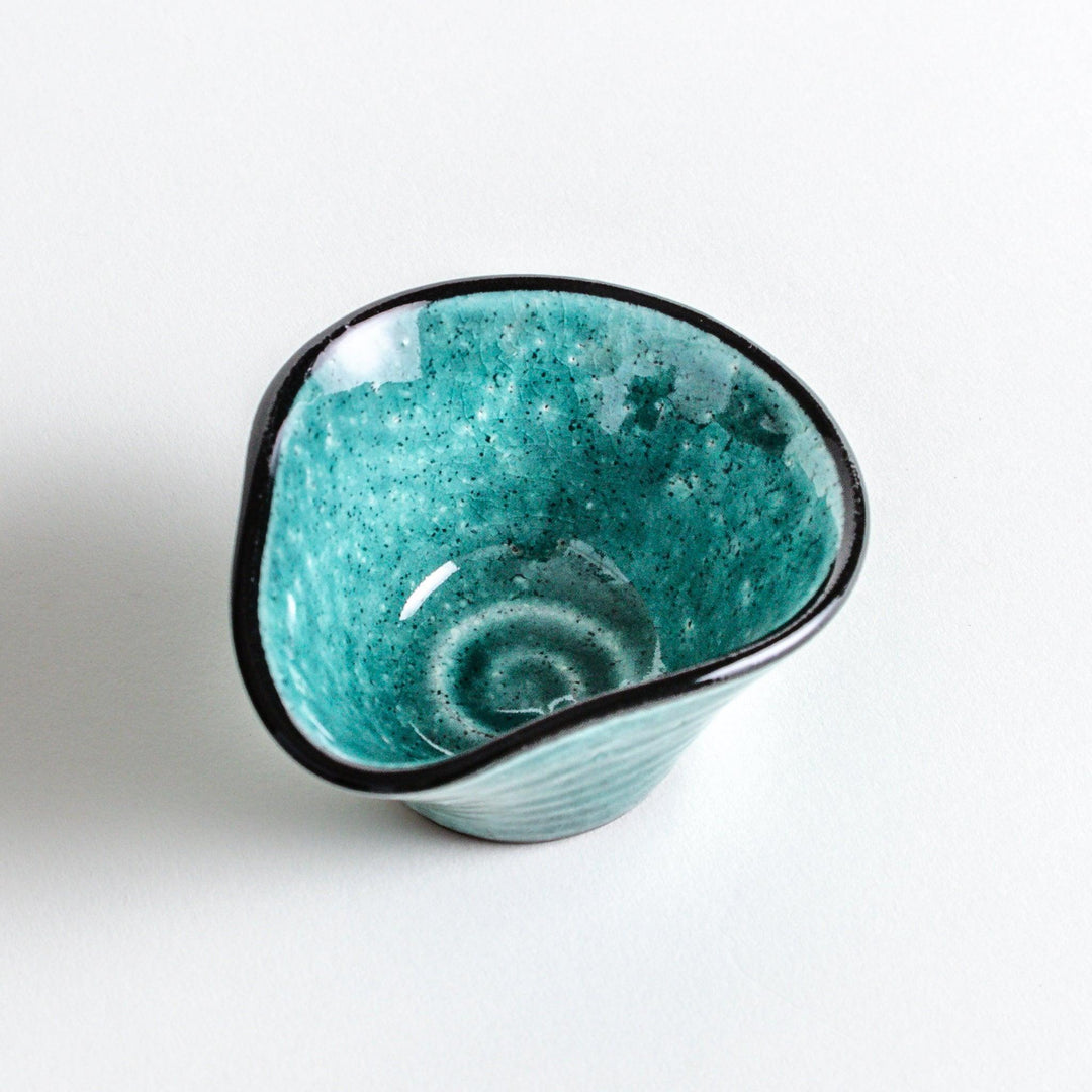 A small condiment bowl in vibrant teal with a black rim.