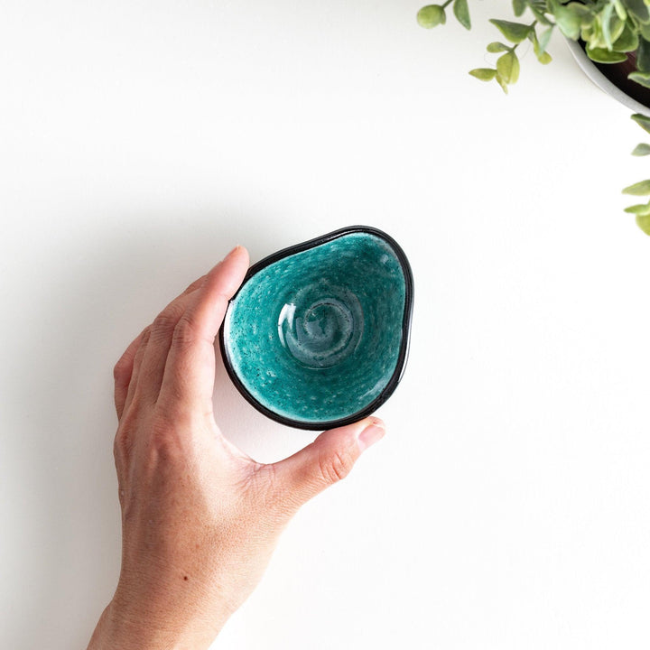 A small condiment bowl in vibrant teal with a black rim.