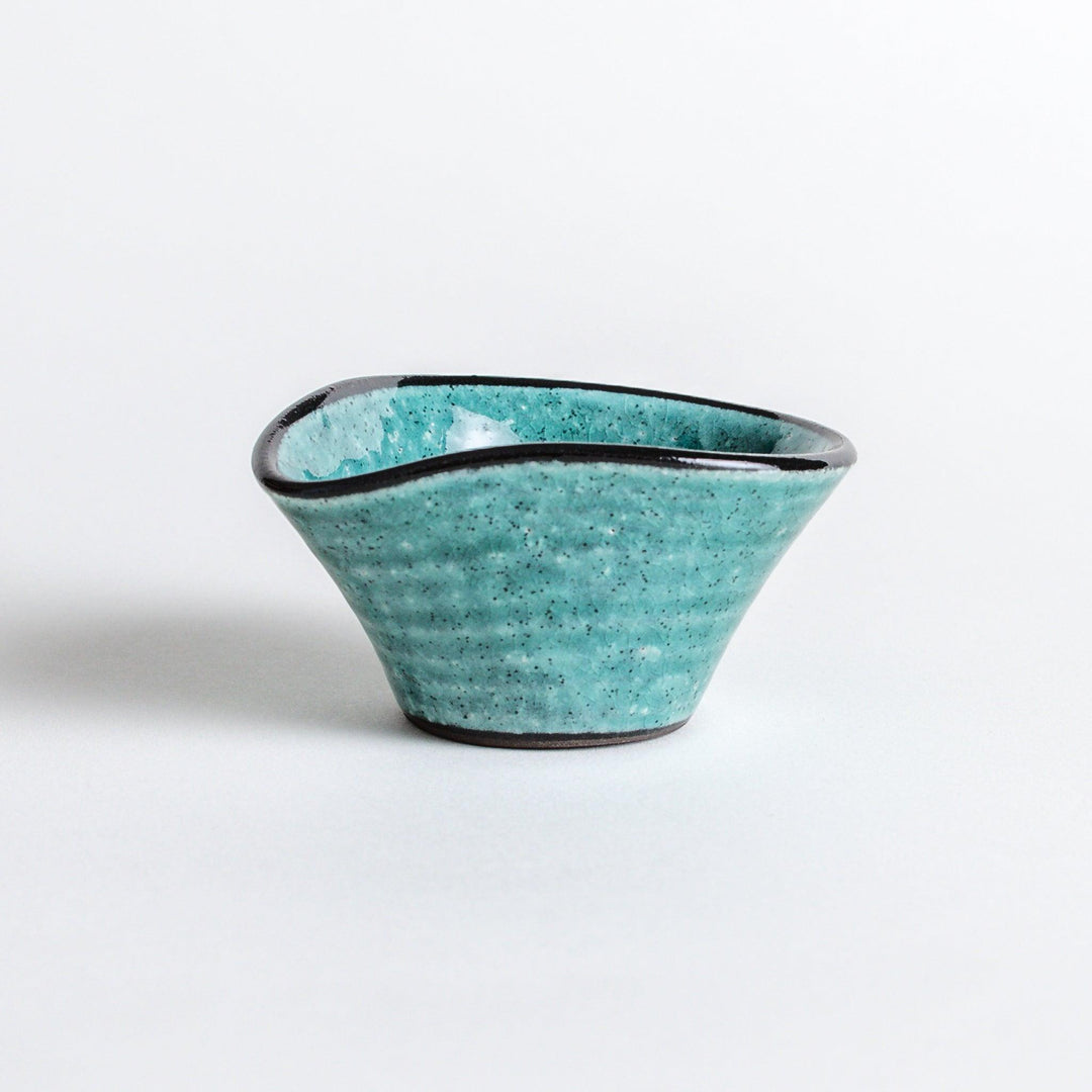 A small condiment bowl in vibrant teal with a black rim.