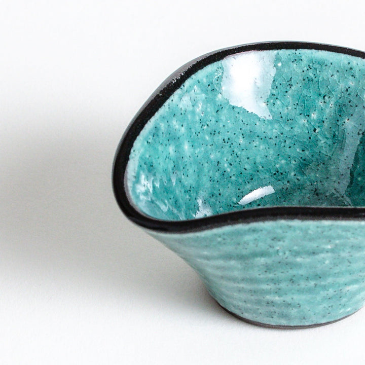 A small condiment bowl in vibrant teal with a black rim.