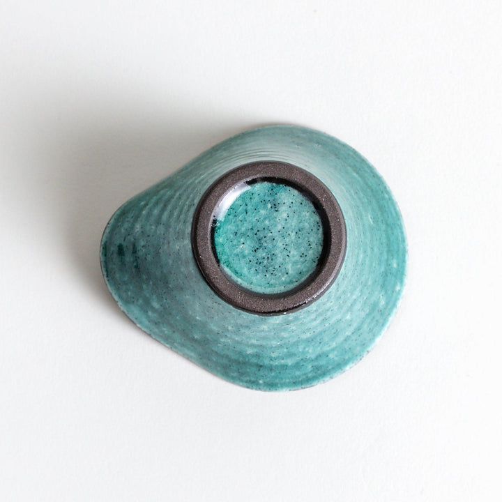 A small condiment bowl in vibrant teal with a black rim.