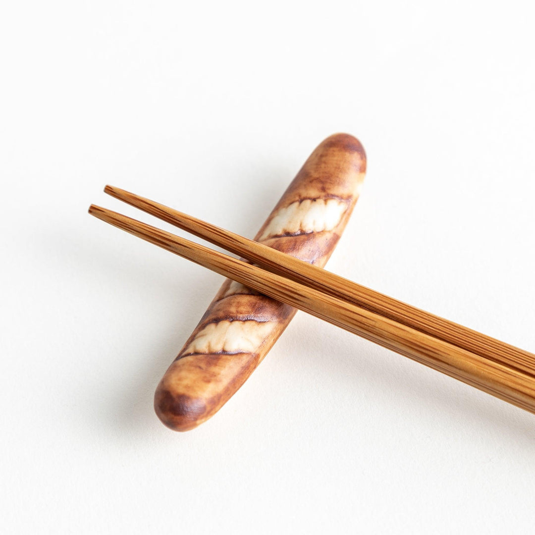 A ceramic chopstick rest designed to resemble a miniature baguette.\