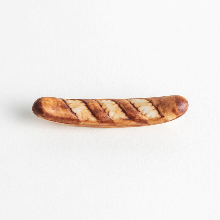 A ceramic chopstick rest designed to resemble a miniature baguette.\