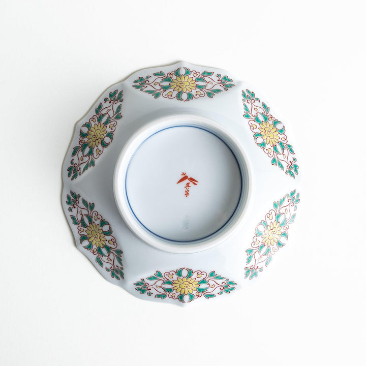 A blue dessert plate with a geometric pattern in the center, accented by ornate floral designs in red, green, and gold on the scalloped rim.