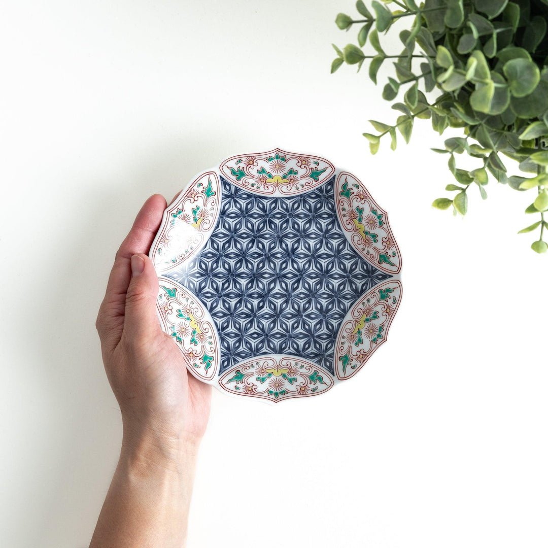 A blue dessert plate with a geometric pattern in the center, accented by ornate floral designs in red, green, and gold on the scalloped rim.