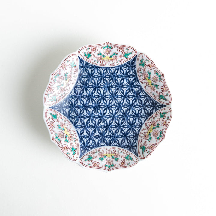 A blue dessert plate with a geometric pattern in the center, accented by ornate floral designs in red, green, and gold on the scalloped rim.