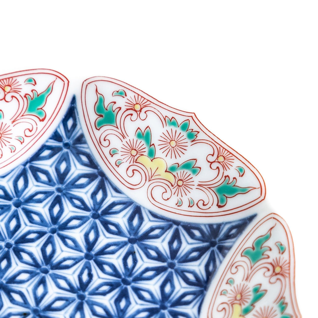 A sauce dish with a blue geometric pattern in the center and ornate floral designs in red, green, and gold on the scalloped rim.