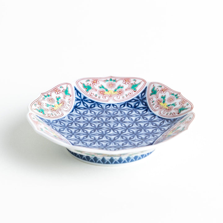 A sauce dish with a blue geometric pattern in the center and ornate floral designs in red, green, and gold on the scalloped rim.