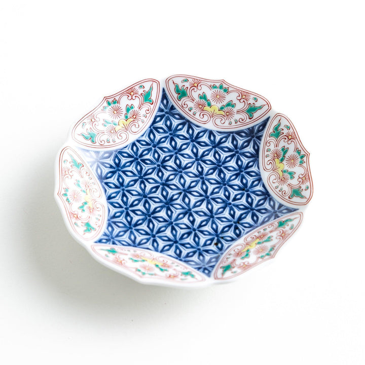 A sauce dish with a blue geometric pattern in the center and ornate floral designs in red, green, and gold on the scalloped rim.