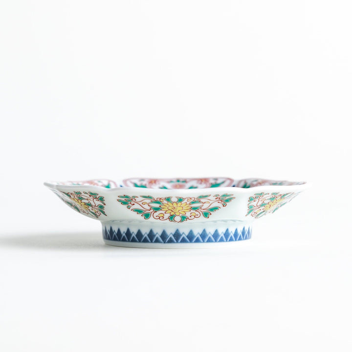 A sauce dish with a blue geometric pattern in the center and ornate floral designs in red, green, and gold on the scalloped rim.